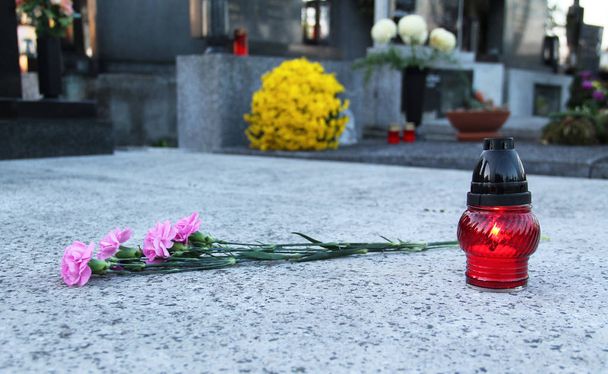 κόκκινο φανάρι με κερί και μάτσο ροζ μοσχοκάρφια (γαρύφαλλα) στον τάφο - Φωτογραφία, εικόνα