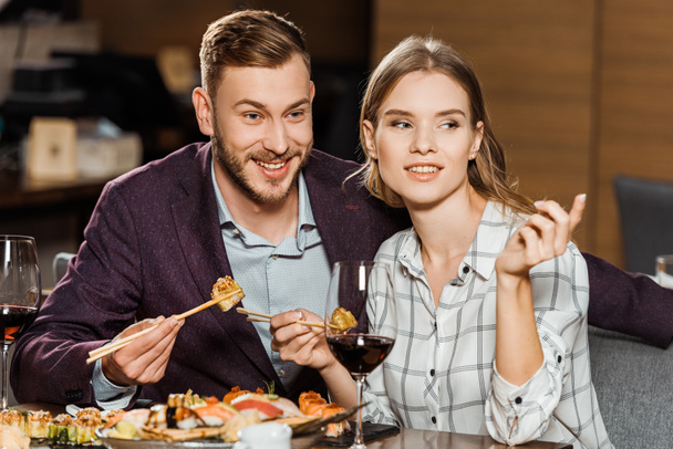 Sorrindo jovem casal adulto comer rolos de sushi no restaurante
 - Foto, Imagem