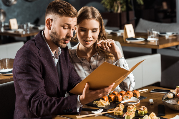 Beautiful young adult couple looking in menu to order dinner in restaurant - Foto, afbeelding