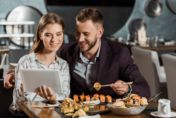 Attractive couple using digital tablet while eating sushi in restaurant - Photo, Image