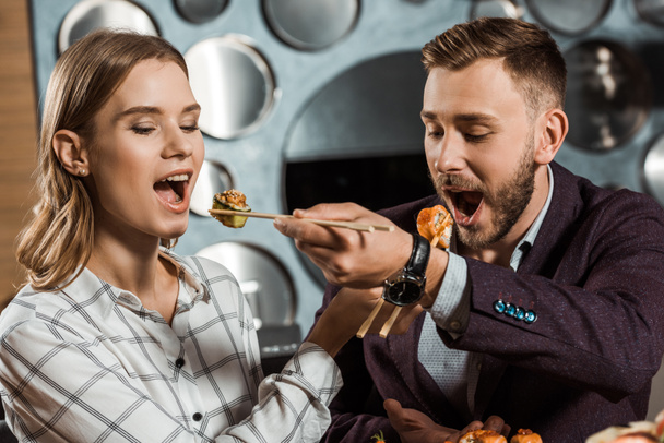 Beautiful couple of young adult feeding each other with sushi in restaurant - Photo, Image
