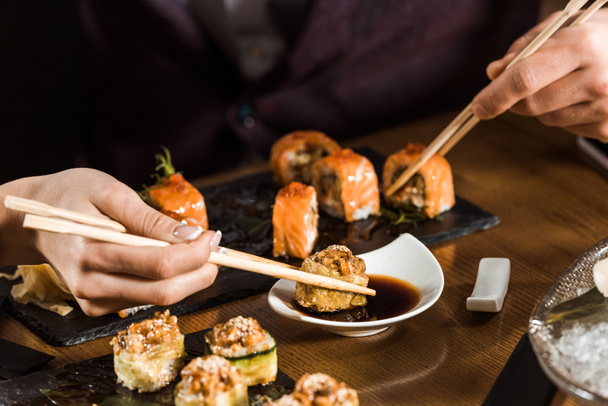 Cropped view of people eating sushi with chopsticks in restaurant - Fotó, kép