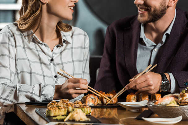 Partial view of smiling couple eating sushi in restaurant - Fotó, kép