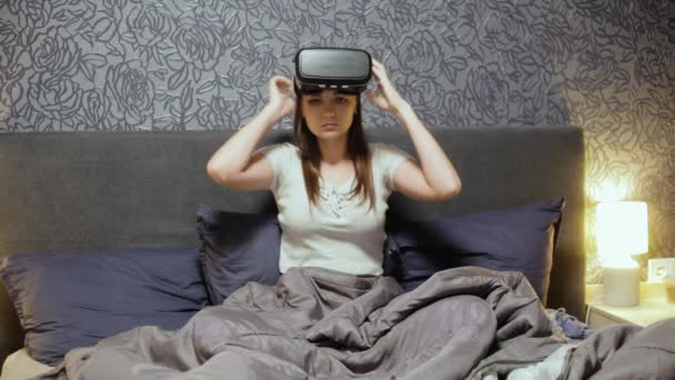 Beautiful young woman wearing VR Headset on the bed. Looking around, smile and using gestures with hands. Watch VR video, play VR game. - Video
