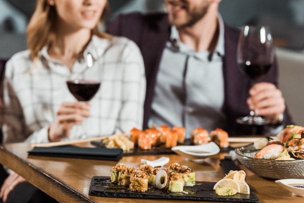 寿司を食べたり、レストランで日付を持ちながらワインを飲むカップルの部分的なビュー - 写真・画像