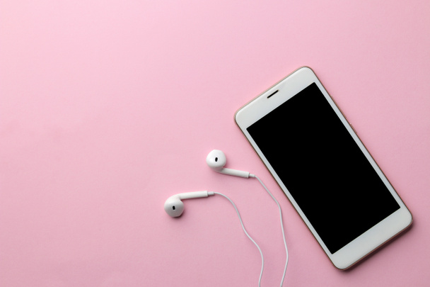 White smartphone with headphones on a bright pink background. view from above - Photo, Image