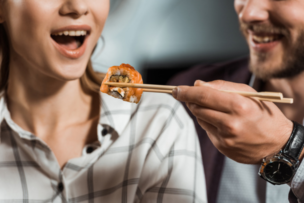 Vista parcial do homem alimentando sua namorada com rolo de sushi
 - Foto, Imagem
