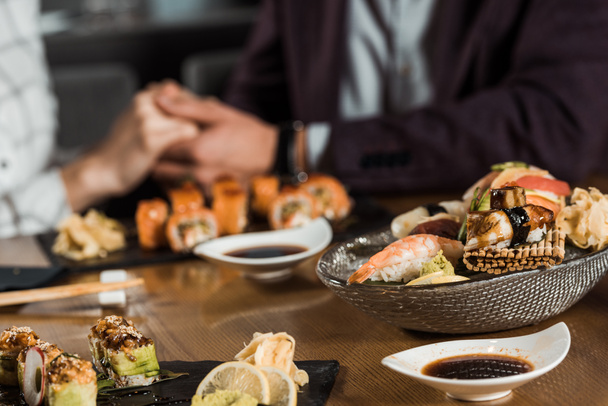 Sushi rolls and seafood on the background of couple holding hands - Photo, Image