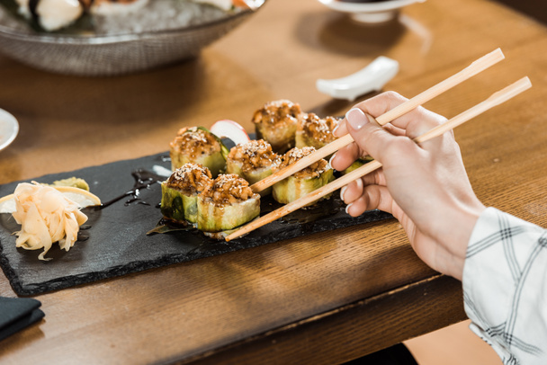 Cropped view of woman holding sushi with chopsticks in restaurant - Photo, Image