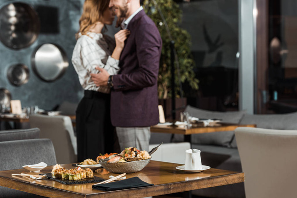 Vista parziale di una bella coppia di abbracci che balla dietro il tavolo servita con sushi nel ristorante
 - Foto, immagini
