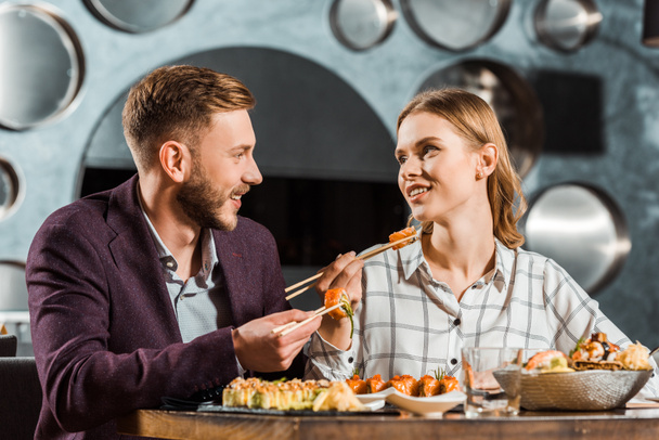 glückliches junges erwachsenes Paar schaut einander beim gemeinsamen Abendessen im Restaurant an  - Foto, Bild
