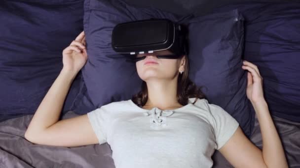 Вид молодой женщины, лежащей на подушках на кровати с помощью виртуальной реальности, смотрите видео
 - Кадры, видео
