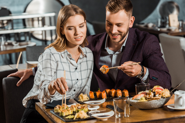 Feliz joven y sonriente pareja adulta comiendo rollos de sushi en el restaurante
  - Foto, imagen