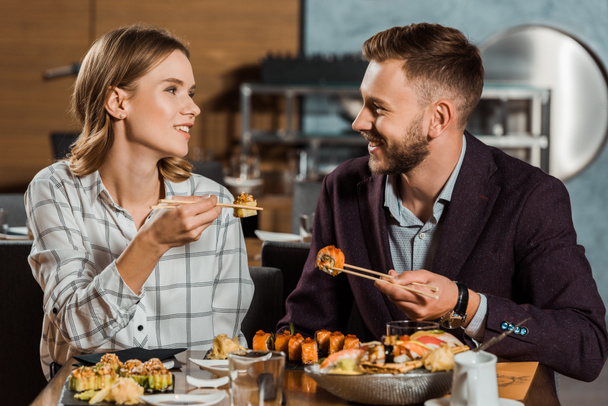 Lovely couple amorously looking at each other and eating sushi rolls in restaurant  - 写真・画像
