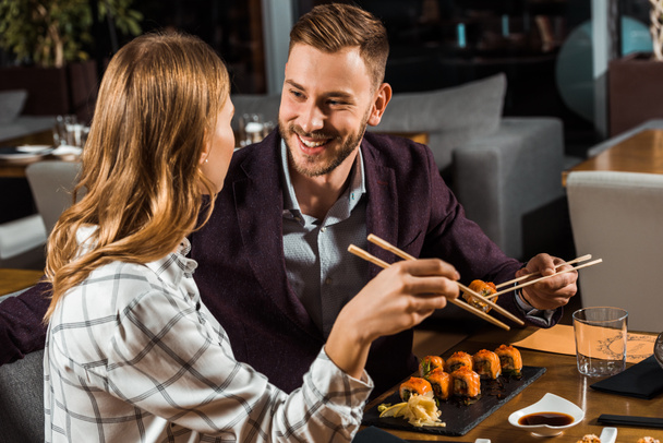 Beautiful happy couple eating sushi rolls in restaurant  - 写真・画像