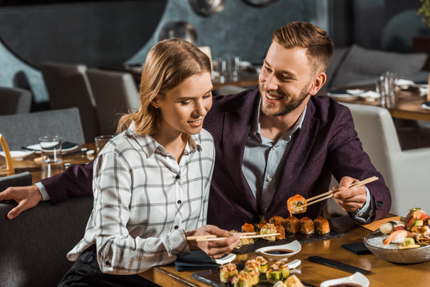 Attractive happy young adult couple eating sushi in restaurant - Photo, Image