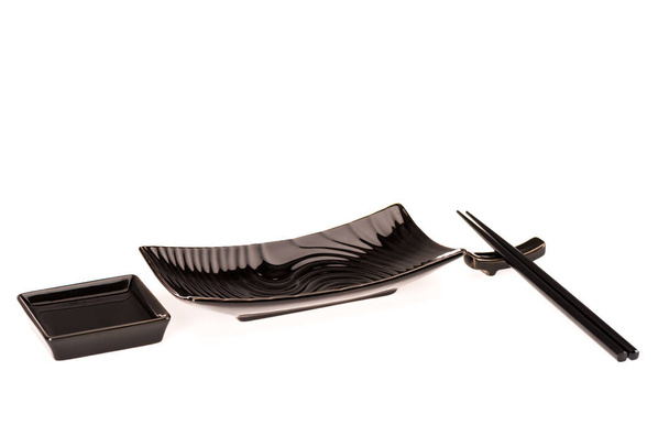 schwarze Teller für Sushi-Rollen und Sojasauce mit Essstäbchen isoliert auf weiß - Foto, Bild