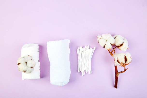 Branch of cotton plant, eared sticks, cotton pads, towel, cosmetic makeup removers tampons, hygienic sanitary swabs  on purple background Top view. Spa concept. Flat lay. Copy space. - Фото, зображення
