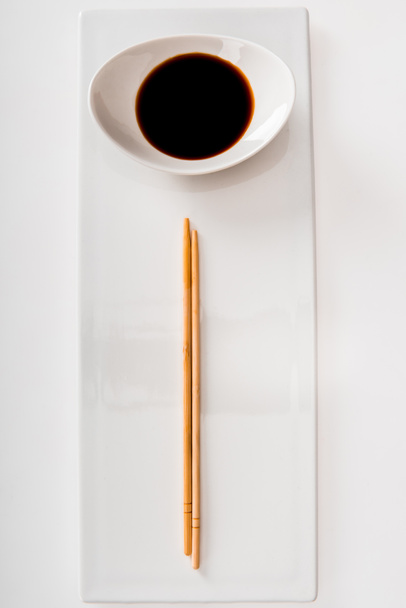 Soya sosu ve yemek çubukları ile plaka üstten görünüm üzerinde beyaz kayrak - Fotoğraf, Görsel