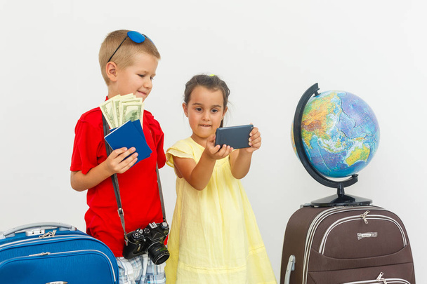 little children with suitcases, dollars and globe on white background, travel concept - Photo, Image