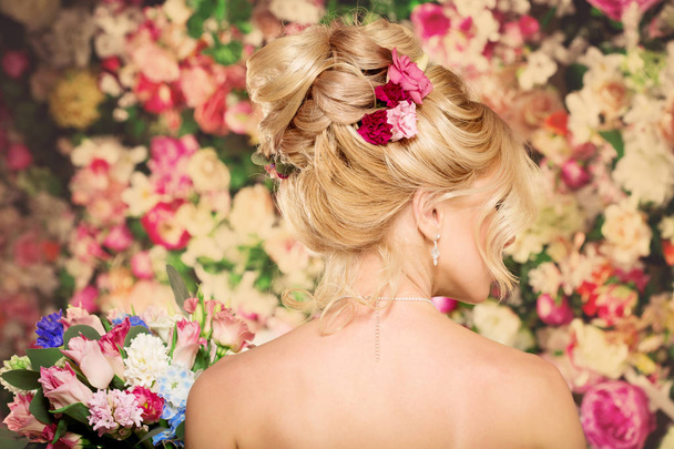Wedding hairstyle a young girl. Bride. Woman with Flowers in her hair. High stacking, a bundle of curls. Beautiful blonde model. Earrings and bouquet - Photo, image