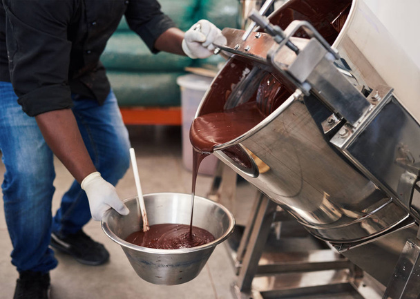 Primer plano de un trabajador en una fábrica de fabricación de chocolate artesanal vertiendo chocolate derretido de una batidora en un tazón
 - Foto, imagen