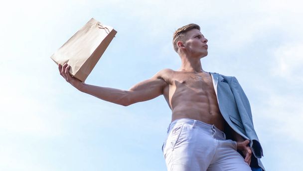 Sales season. Take this package. Shop assistant concept. Man muscular athlete hold shopping bag sky background. Hot sales and discount. Guy attractive macho carry shopping bag made out of brown paper - Foto, imagen