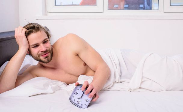 Sleep regime habit. Man unshaven lay bed hold alarm clock. Man unshaven bearded wakeful face having rest. Stick schedule same bedtime wake up time. Enough sleep for him. Regulate your bodys clock - Фото, зображення