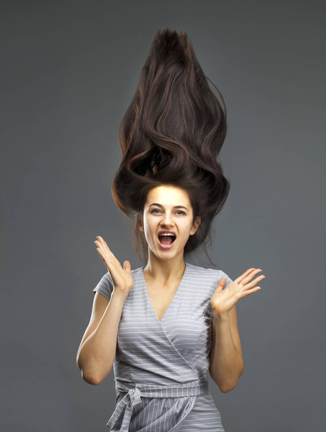 Portrait of a beautiful brunette woman with hair up in the air isolated on gray background - 写真・画像