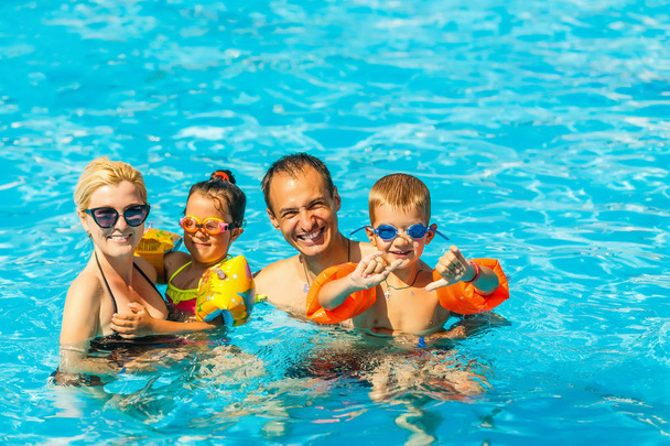 Χαρούμενη οικογένεια με δύο παιδιά που διασκεδάζουν στην πισίνα - Φωτογραφία, εικόνα