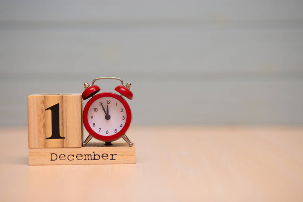 1 de diciembre fijado en calendario de madera y reloj despertador rojo con fondo azul. Cara de reloj mostrando cinco minutos hasta la medianoche
 - Foto, Imagen