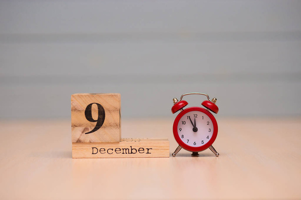 09 de dezembro definido no calendário de madeira e despertador vermelho com fundo azul. Cara do relógio mostrando cinco minutos para a meia-noite
 - Foto, Imagem