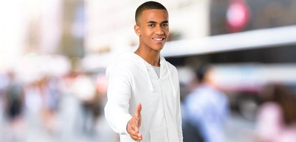 Jovem de pele escura com camisola branca handshaking depois de um bom negócio no exterior
 - Foto, Imagem