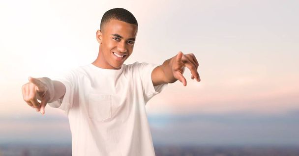 Νεαρός αφρικανική αμερικανική άνθρωπος σημεία το δάχτυλό σας ενώ χαμογελά σε φόντο ηλιοβασίλεμα - Φωτογραφία, εικόνα