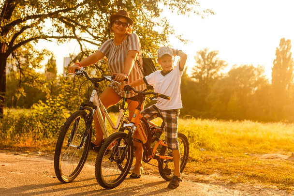 Happy woman with son riding bikes at sunset - Fotó, kép