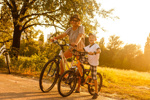 Happy woman with son riding bikes at sunset - Photo, Image