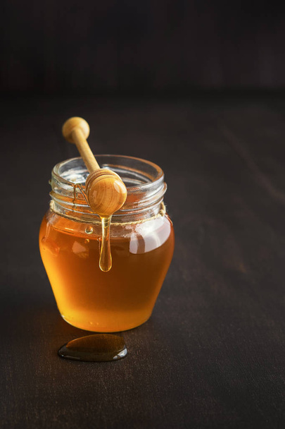 Honey in a glass jar with honey dipper on rustic wooden table background. Copy space. Vertical. - 写真・画像