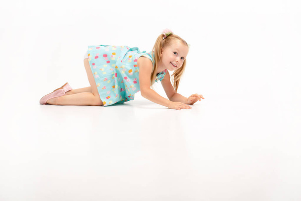 cute beautiful little blonde girl crawls on her knees, she rests with their. Isolate on white background - Photo, Image