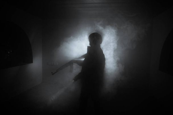 アサルトライフルの暗いトーンの霧の背景または危険な山賊の手に銃を保持している攻撃する準備を持つ男のシルエット。武器のテーマの装飾が施されたテロリストを撮影 - 写真・画像