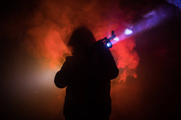 Silhouet van man met assault rifle klaar om te vallen op donker getinte mistige achtergrond of gevaarlijke bandit pistool in de hand te houden. Schieten terrorist met wapen thema inrichting - Foto, afbeelding