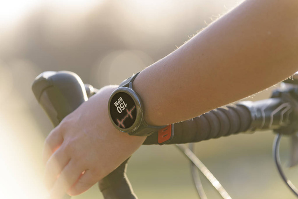 Mujer montando una bicicleta y usando smartwatch al monitor de frecuencia cardíaca
 - Foto, imagen