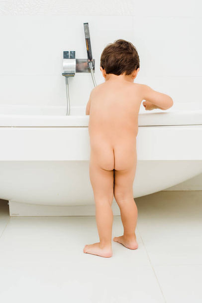 Γυμνό παιδί αγόρι στέκεται στο λευκό μπάνιο - Φωτογραφία, εικόνα