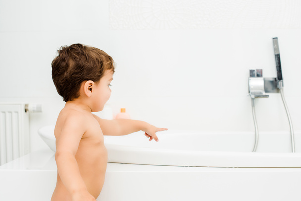 Menino de criança apontando para torneira no banheiro branco
  - Foto, Imagem