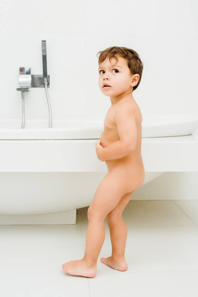 Small naked kid standing in white bathroom - Фото, изображение