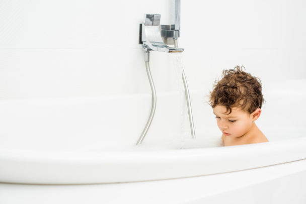 Pikkulapsi poika istuu kylpyhuoneessa juoksevalla vedellä
 - Valokuva, kuva