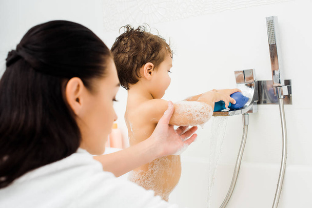 Moeder die hand van zoon spelen in witte badkamer  - Foto, afbeelding