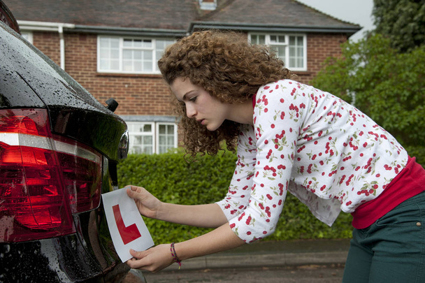 Young female driver attaching a L plate on the rear of a car - Photo, Image