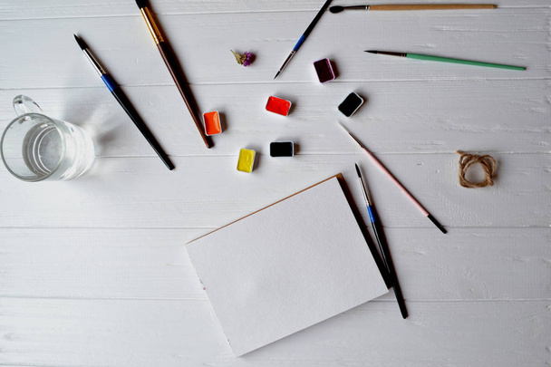 Εργαλεία για τη ζωγραφική στο λευκό ξύλινο γραφείο. Πινέλα, χαρτί και χρώματα στο τραπέζι. Στο χώρο εργασίας του ζωγράφου. - Φωτογραφία, εικόνα