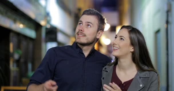 Front view of a happy couple walking towards camera sightseeing in the night in the street - Кадри, відео