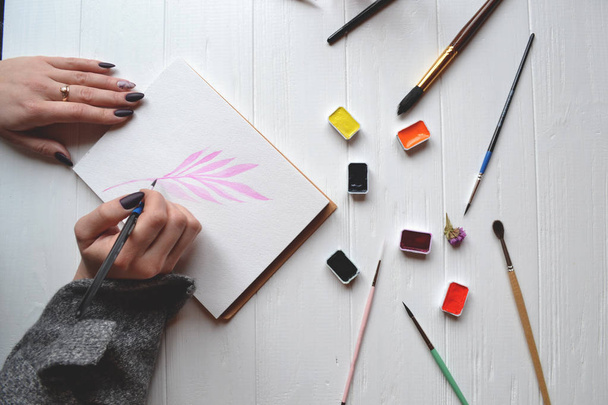 Une femme peint dans un carnet de croquis. Outils pour peindre sur le bureau en bois blanc. Travail de peintre
. - Photo, image